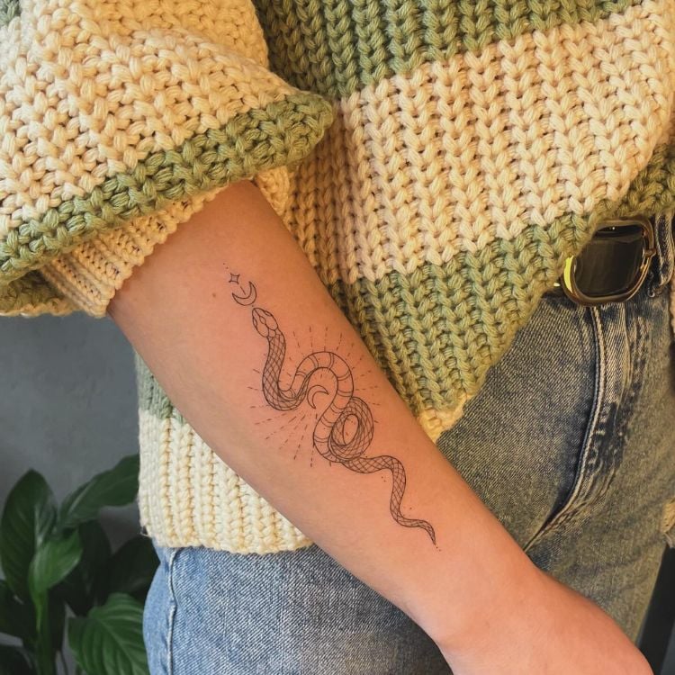 um braço feminino com uma tatuagem de cobra  com duas meia luas