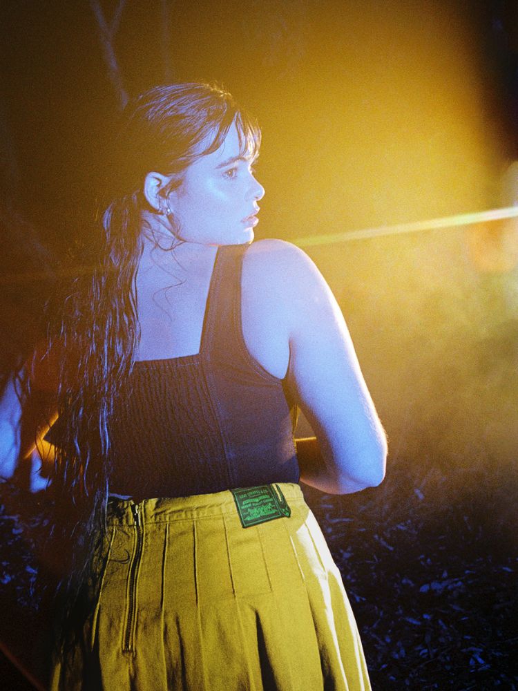 A atriz usando o corset e a saia amarela olhando sobre o ombro