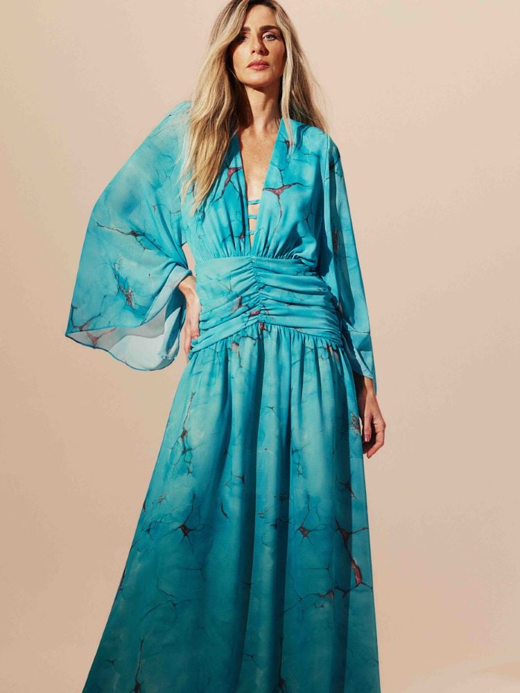 Mariana Weickert usando vestido azul turquesa  longo com detalhes em dourado, drapeado e com manga flare. 