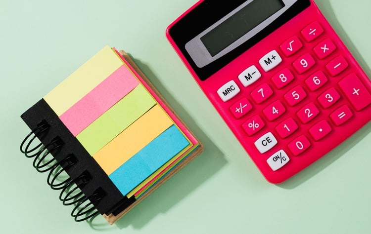 calculadora rosa com um mini caderno com post it coloridos ao lado