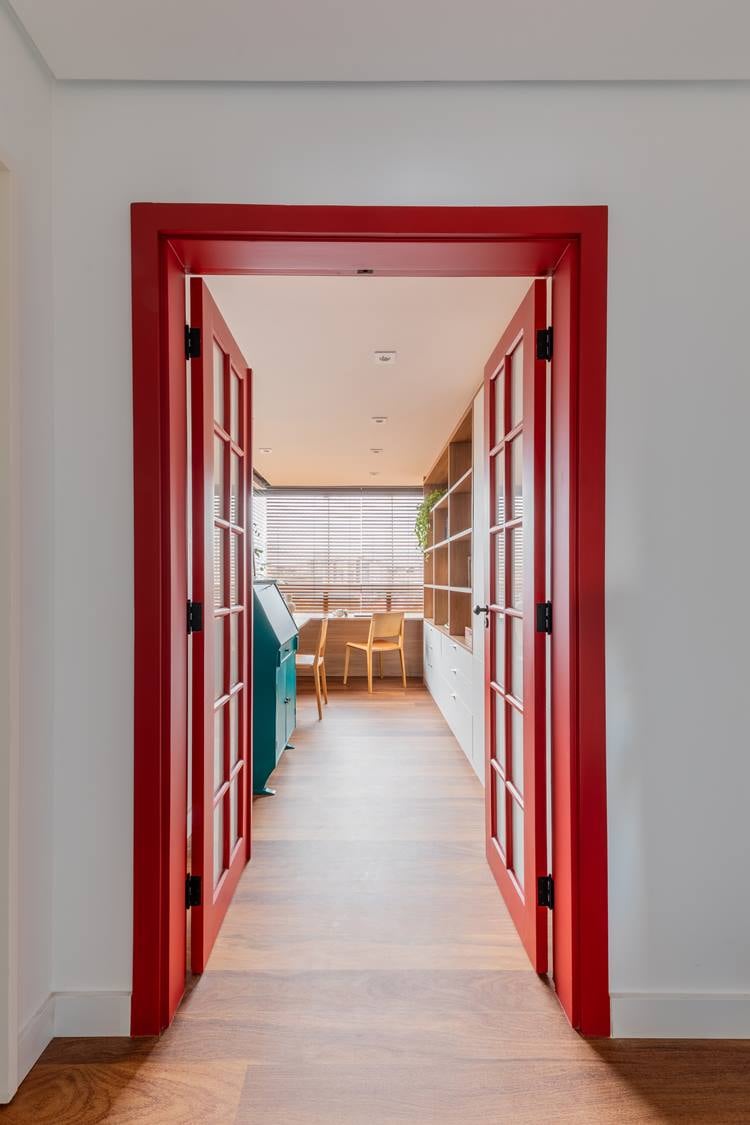 Porta vermelha de vidro e duas repartições aberta dá entrada para escritório.