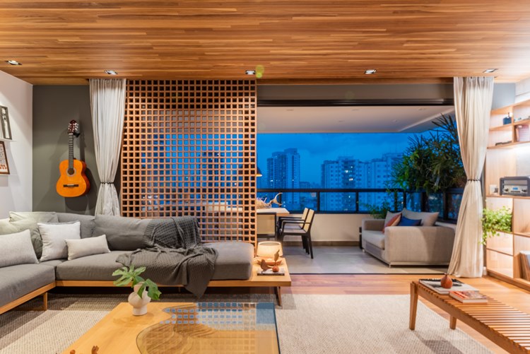 Sala de estar ou living do apartamento decorado de 187 m². Sofá cinza e poltronas com almofadas, integrada com a varanda da casa, com mesa e outro sofá que dá vista à cidade