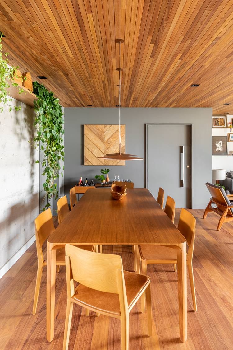 Sala de jantar de apê de 187 m² decorada pelo arquiteto Pietro Terlizzi, com mesa de 8 cadeiras de madeira, prateleira com planta jiboia, e 3 pendentes de luz no centro, no canto um bar móvel, integrada com a sala de estar