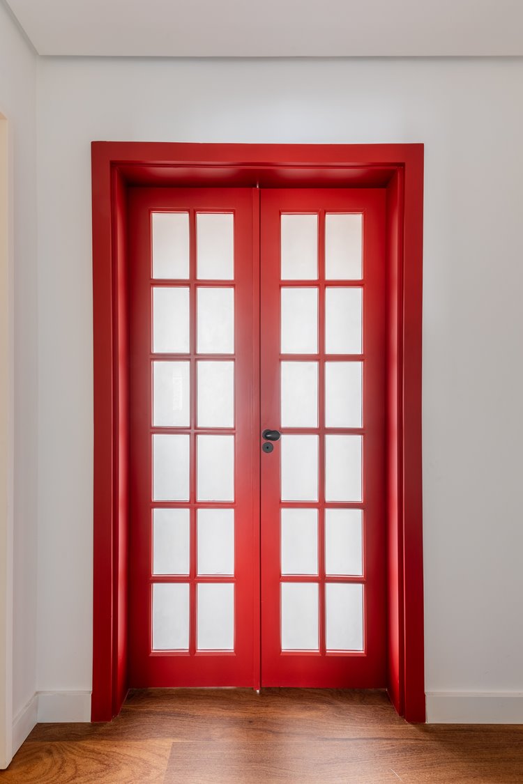 Porta vermelha de vidro e duas repartições fechada em parede branca.