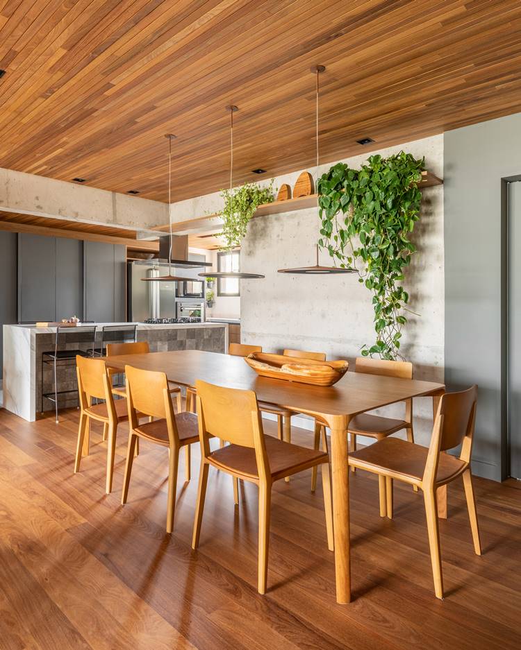 Sala de jantar de apê de 187 m² decorada pelo arquiteto Pietro Terlizzi, com mesa de 8 cadeiras de madeira, prateleira com planta jiboia, e 3 pendentes de luz no centro, integrada com a cozinha