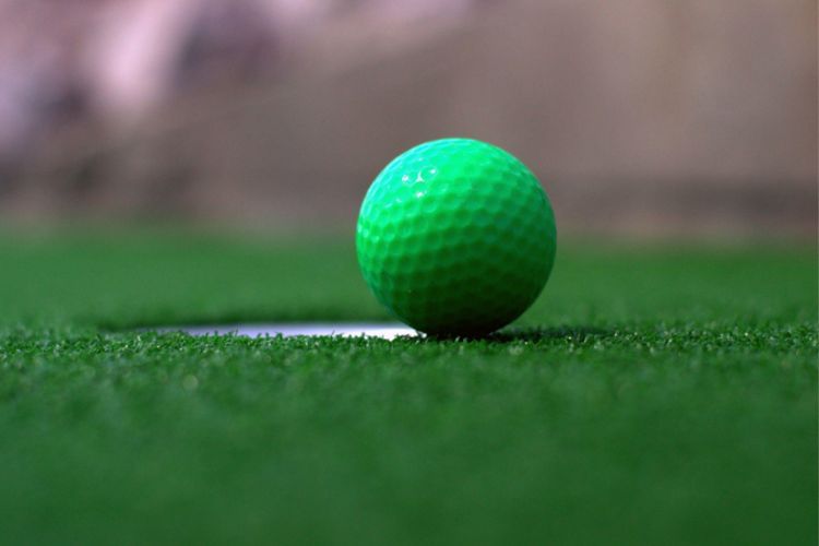 foto de buraco em grama sintética com bola de golfe verde bem na borda