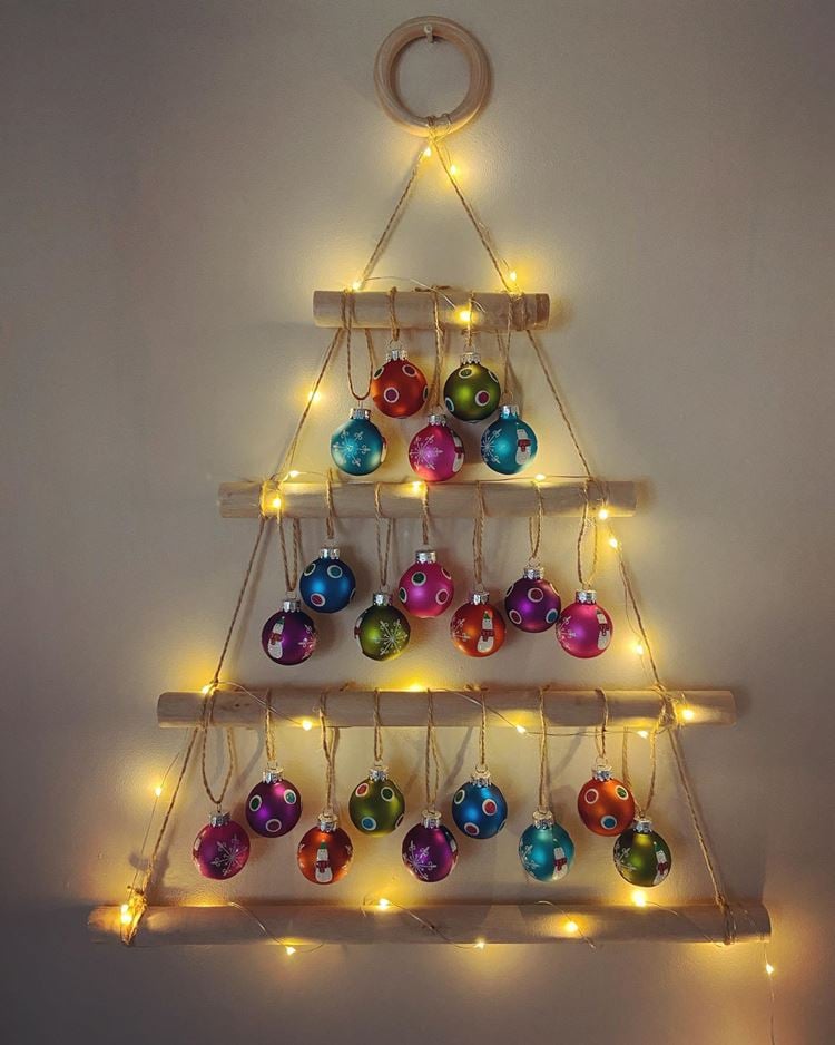 Parede bege com pequena árvore de Natal de madeira, enfeitada com bolas natalinas coloridas: pink, vermelho, verde e azul