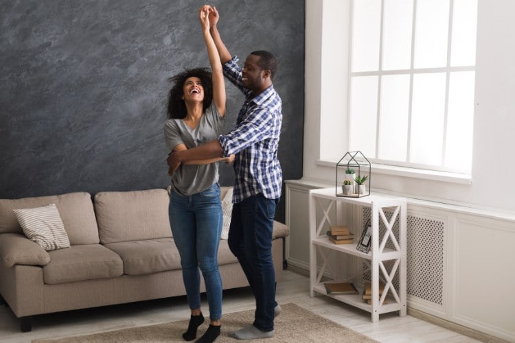 Casal dançando na sala de casa, com sofá e aparador decorado com objetos