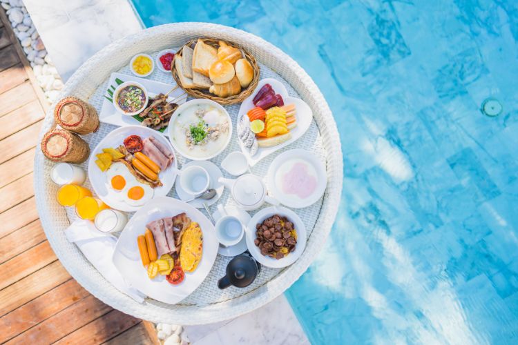 Café da manhã variado, com ovos, frutas e pa~es, servido em uma bandeja próxima à piscina.