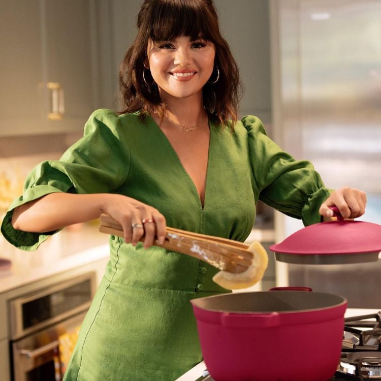 Uma foto da cantora e atriz Selena Gomez usando um vestido verde e cozinhando 