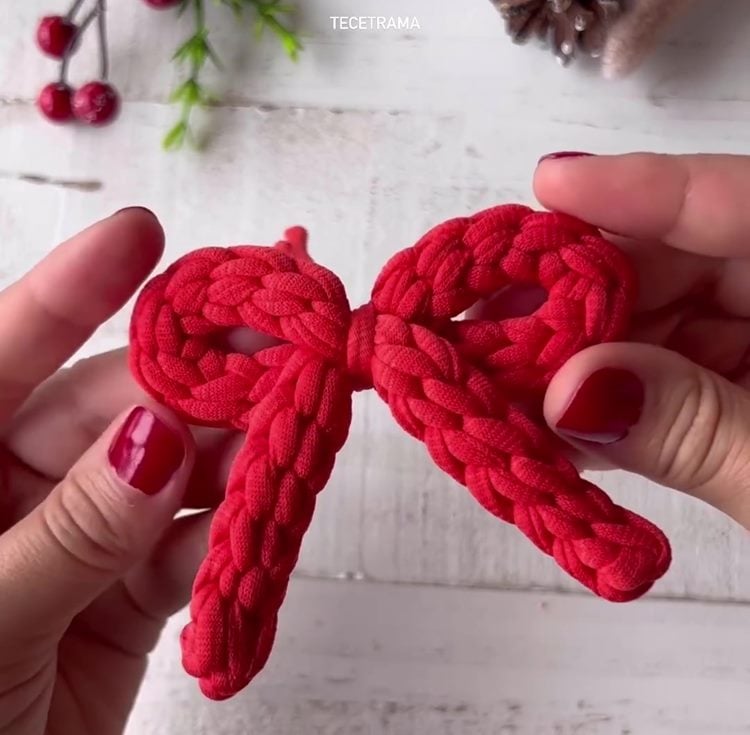 Mãos com unhas vermelhas segurando laço de Natal de crochê vermelho
