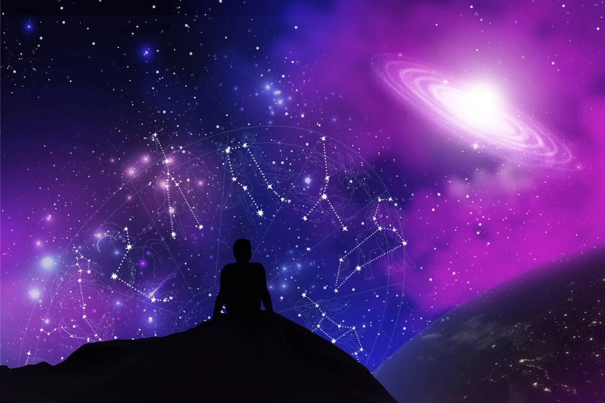 Sombra de uma pessoa sentada no chão olhando para o céu com constelações de signos e Saturno.