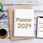 Planner 2024 em mesa de madeira com flores azuis, xícara de café, óculos e celular aberto em planner semanal digital.