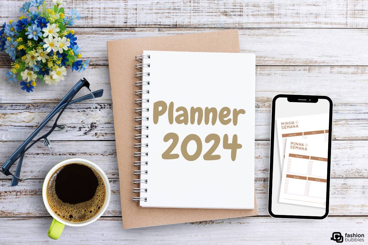 Planner 2024 em mesa de madeira com flores azuis, xícara de café, óculos e celular aberto em planner semanal digital.