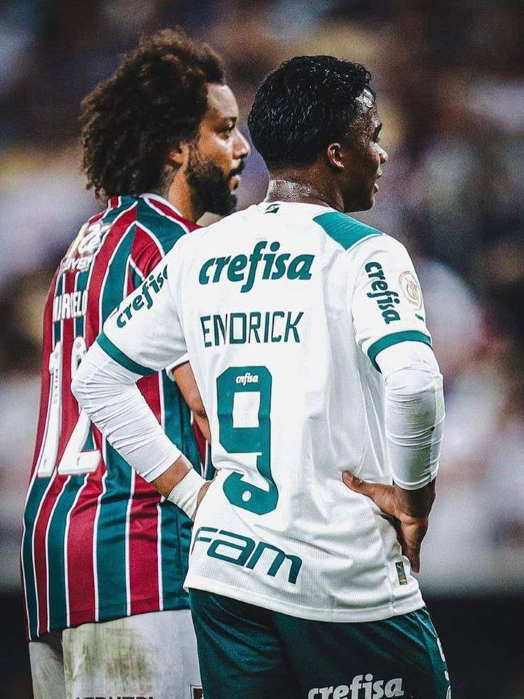 Imagem do lateral tricolor Marcelo, de costas, ao lado do atacante palmeirense Endrick. 