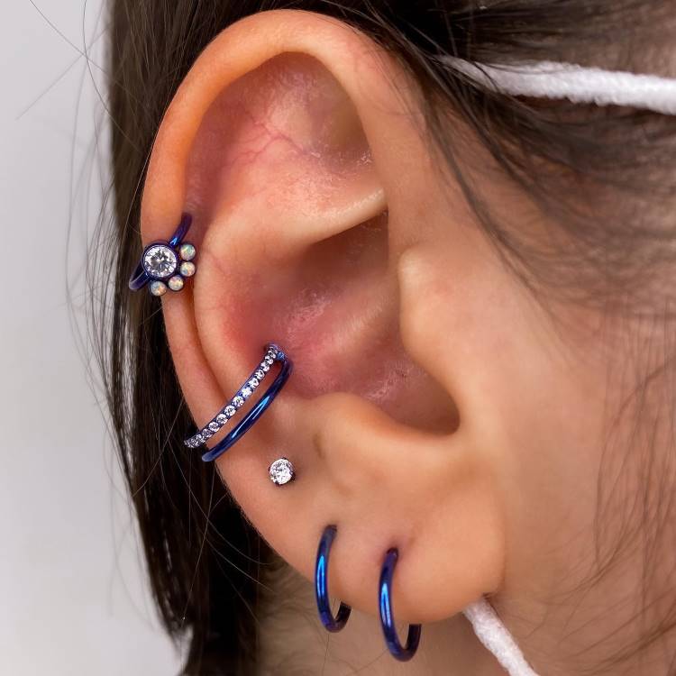 Projeto auricular anodizado em azul, com piercing na hélix, conch e lóbulo. 
