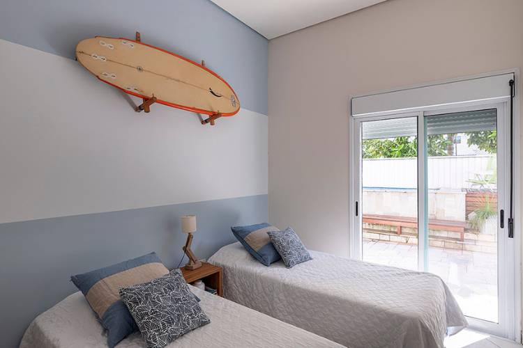 Quarto com duas camas de solteiro, parede azul e branco e prancha de surf. 