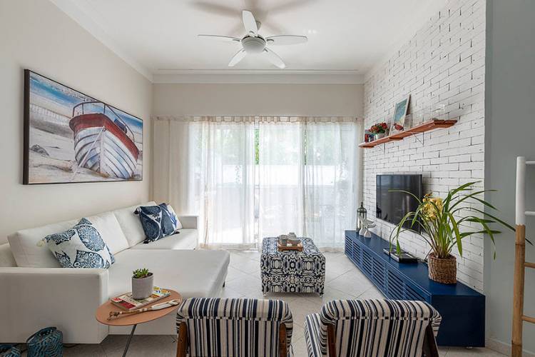 Sala de estar com rack azul, poltronas, sofá branco,  quadro de barco e janela grande. 