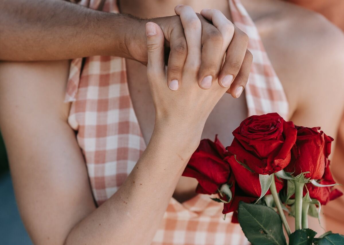 foto de um casal com mão masculina negra segurando uma mão feminina branca com rosas vermelhas ao lado