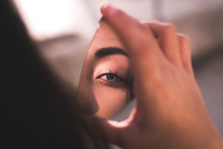 reflexo do olho claro de uma mulher em um pequeno espelho que ela está segurando