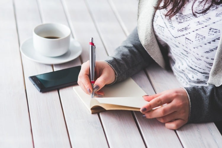 mulher escrevendo em um caderno com uma xícara de café do lado