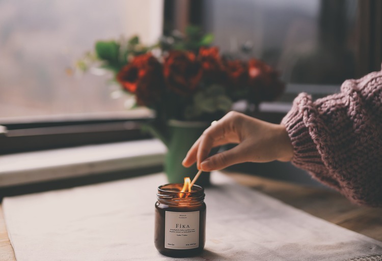 mão feminina acendendo uma vela aromática com rosas atrás que remetem à simpatias para o amor