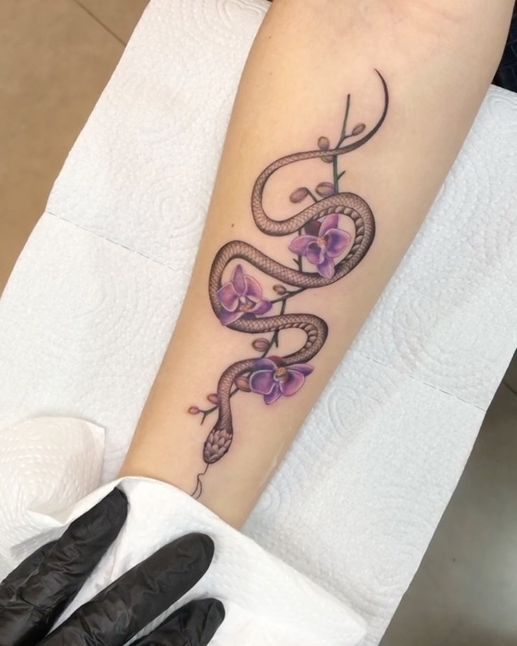 Tatuagem de cobra com flor orquídea lilás no braço