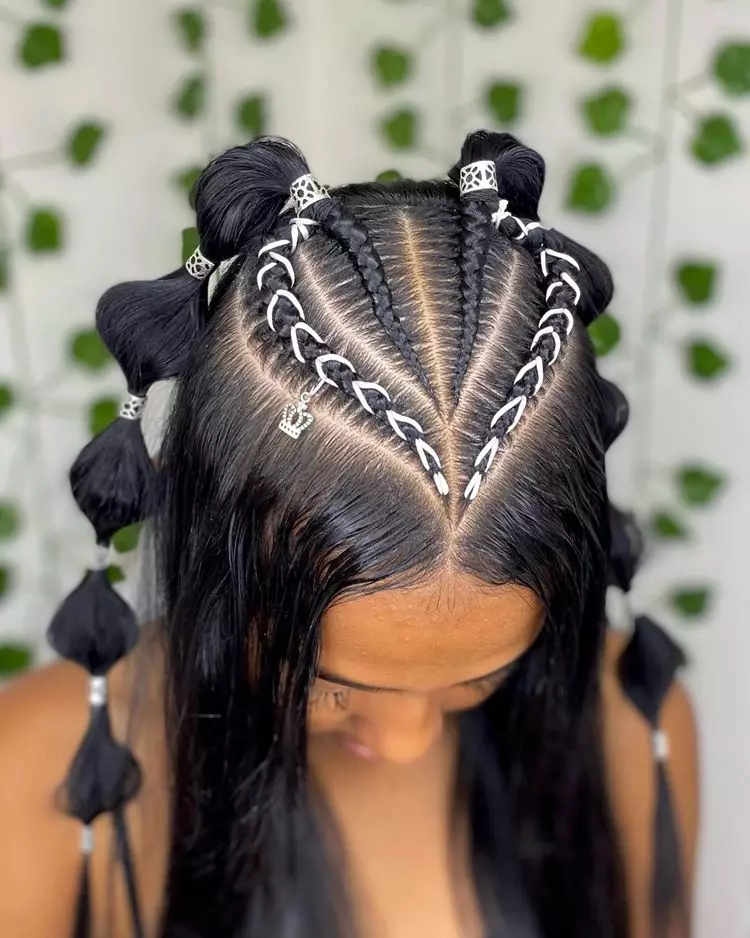 Mulher com a cabeça abaixada mostrando tranças nagô com fio de seda branco e penteado com joias. Ela possui cabelo liso.