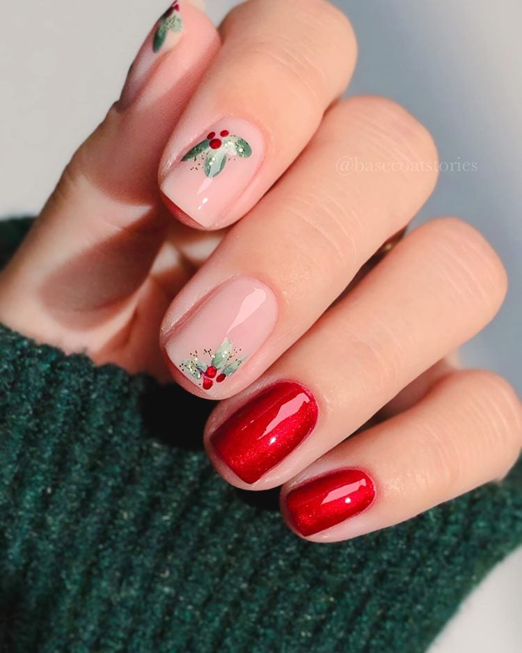 Mão com unhas curtas decoradas para Natal em vermelho brilhante, nude e desenho de planta azedinha