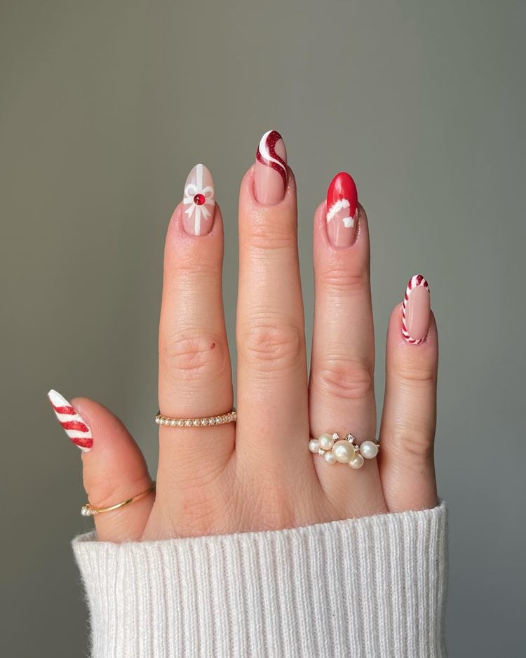 Mão com nail art natalina, vermelho e branco em vários desenhos, como laço, gorro de papai noel e outros