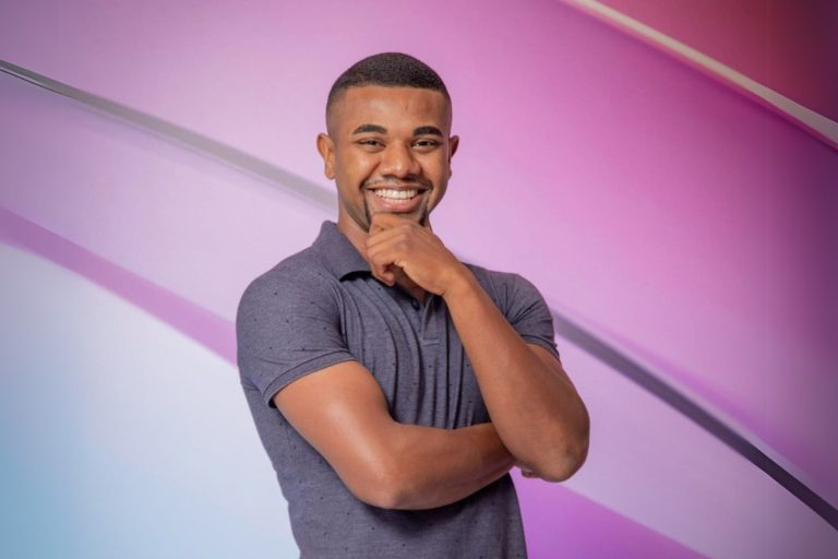 Davi Brito usando camiseta cinza, com mão no queixo, em fundo roxo do BBB