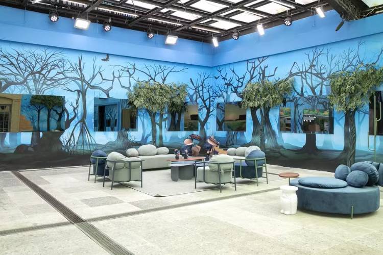 Área externa do BBB 24 com árvores, sofás e parede azul. 