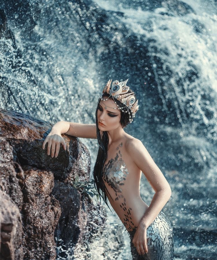 Foto de mulher vestida de sereia apoiando em Pedra de cachoeira
