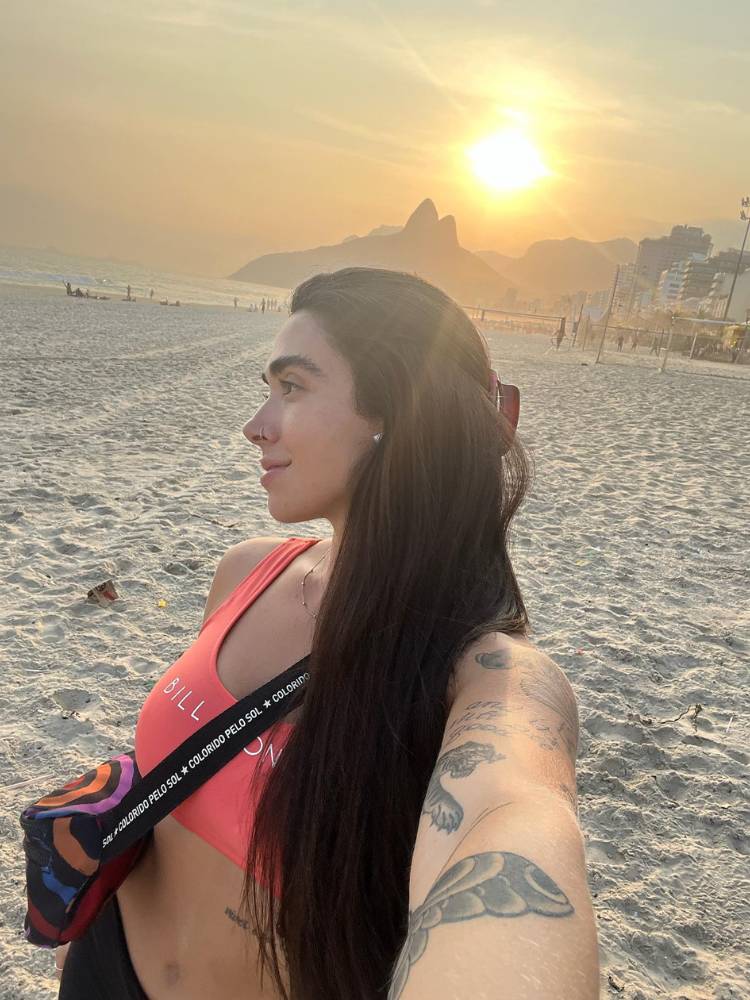Giobanna Lima na praia usando top rosa e exibindo seu longo cabelo castanho escuro liso. 