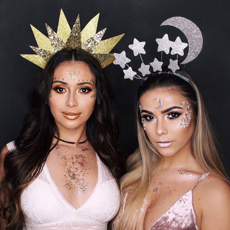 Duas mulheres de pele clara, uma usando tiara de sol e a outra de lua com estrelas.