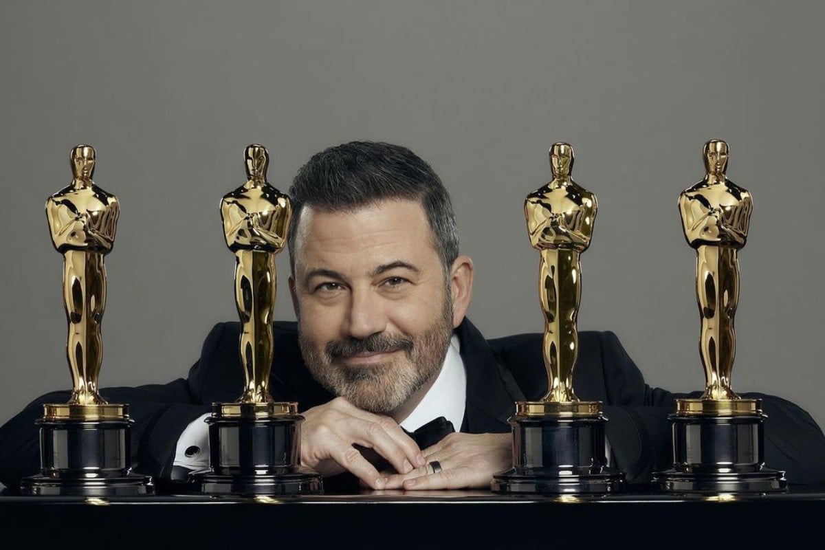 Jimmy Kimmel apoiado no púlpito com 4 estatuetas do Oscar.