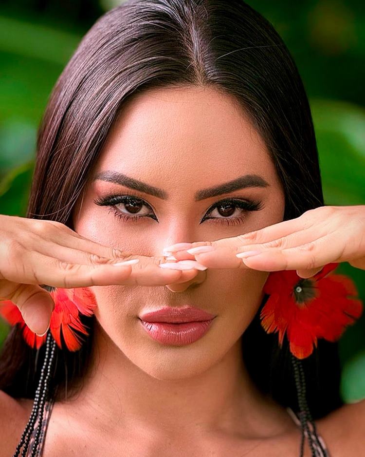 Rosto de Isabelle Nogueira do BBB 24, ela está maquiada, usando brincos de flor vermelha e miçangas, com as mãos abaixo dos olhos, retas em frente ao nariz