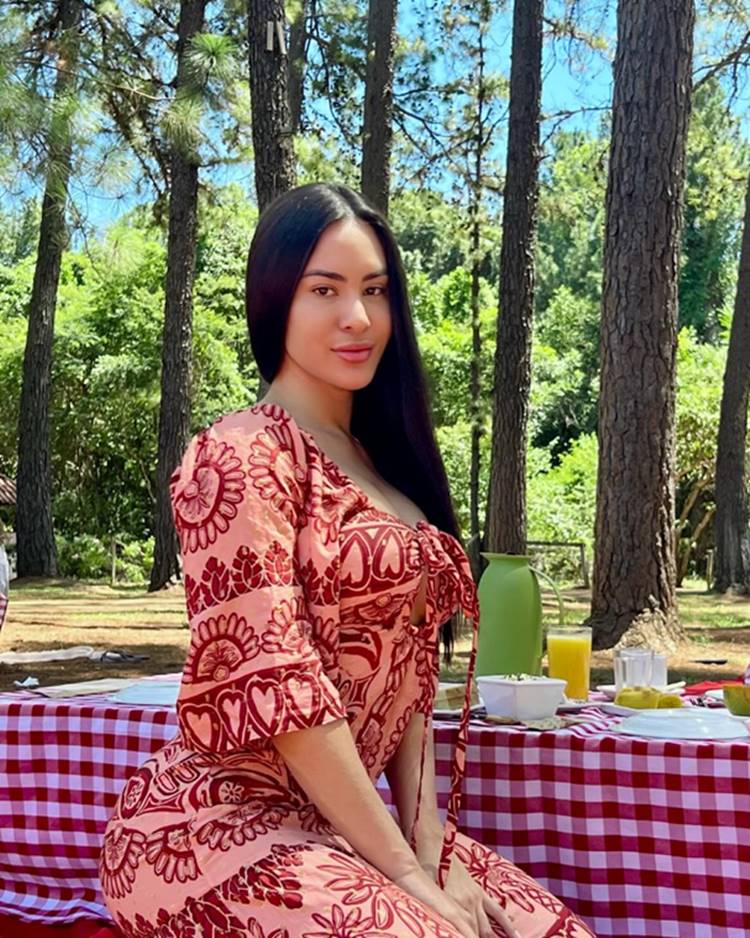 Isabelle Nogueria do BB2 4 usando vestido sentada em frente à mesa com café da manhã ao ar livre em meio á pinheiros