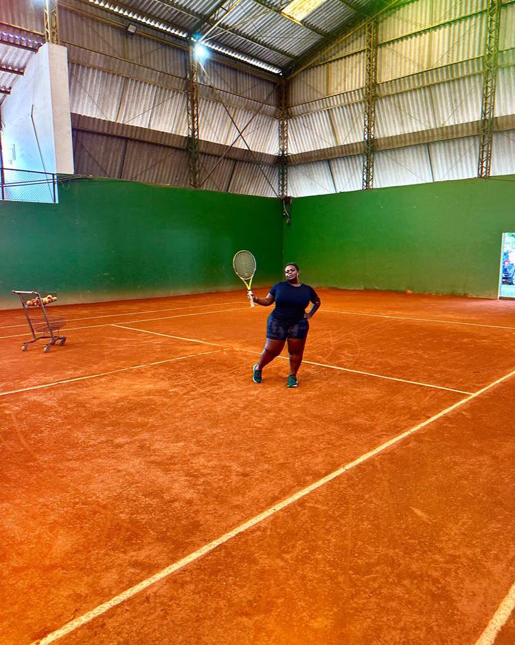 Jojo Todynho praticando tênis em quadra, usando look preto, segurando raquete