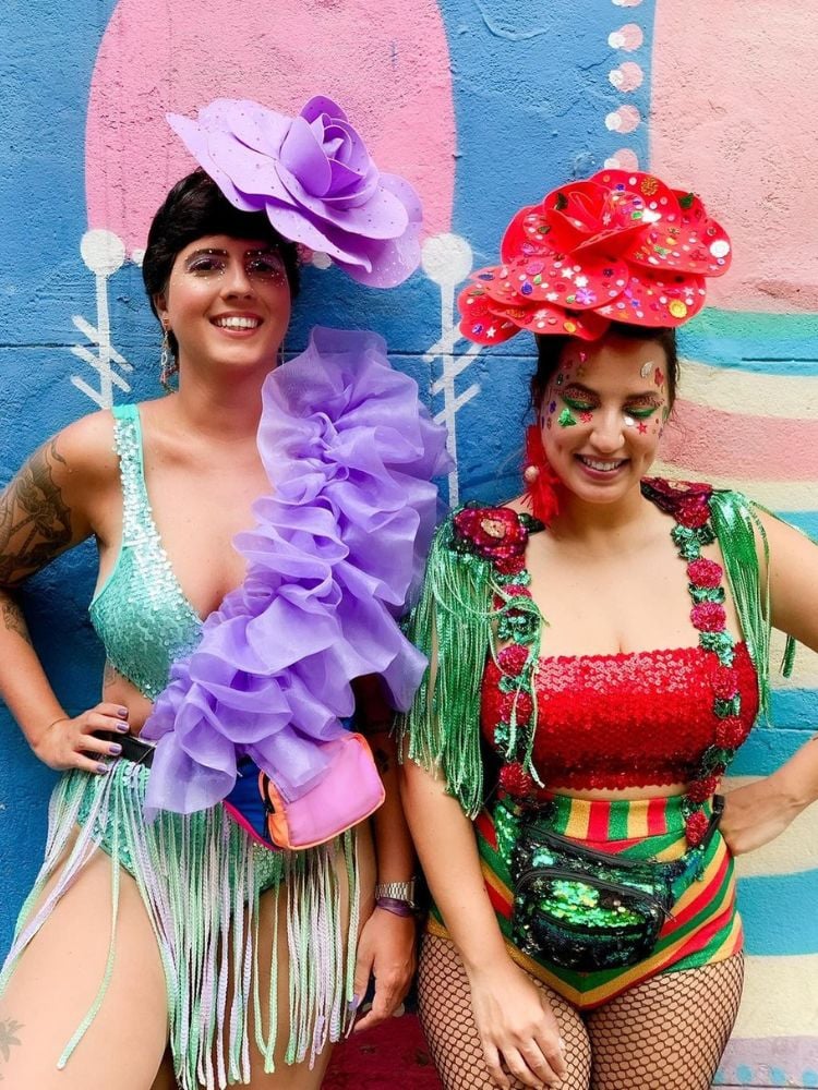 duas amigas usando fantasia de Carnaval 2024 na tendência maximalista, com babados, franjas e tiara de cabeça com flor gigante