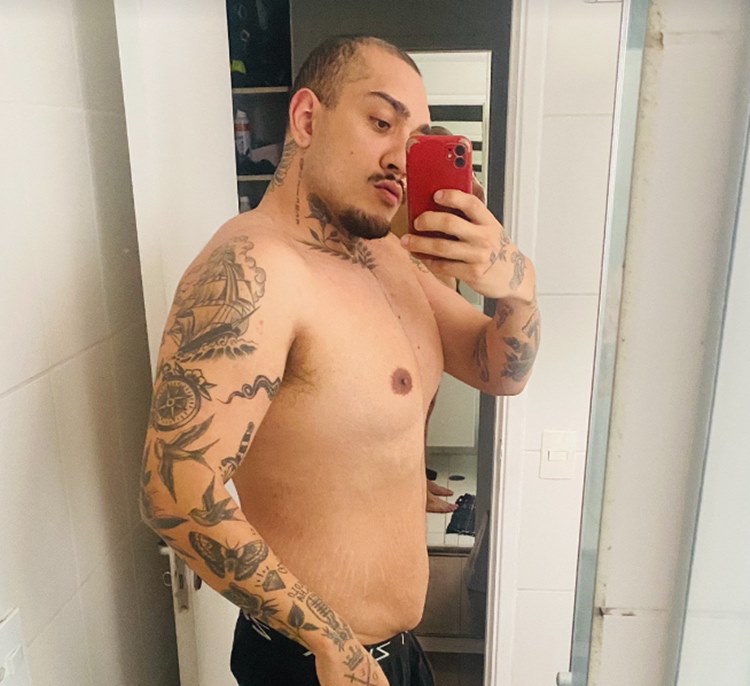 O shape atual de Mc Bin Laden, o participante do BBB 24, tatuado, é revelado em uma selfie no espelho com um iPhone vermelho, possivelmente em um closet. Ele mostra como está sua barriga hoje.