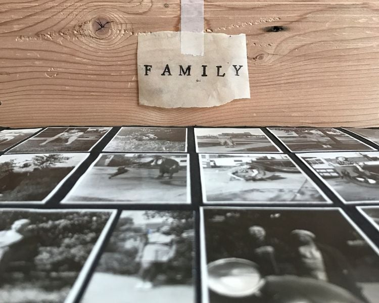 Fotografias antigas preto e branco de pessoas em superfície preta. Em cima, um pedaço de madeira e um papel escrito "Family" colado com fita