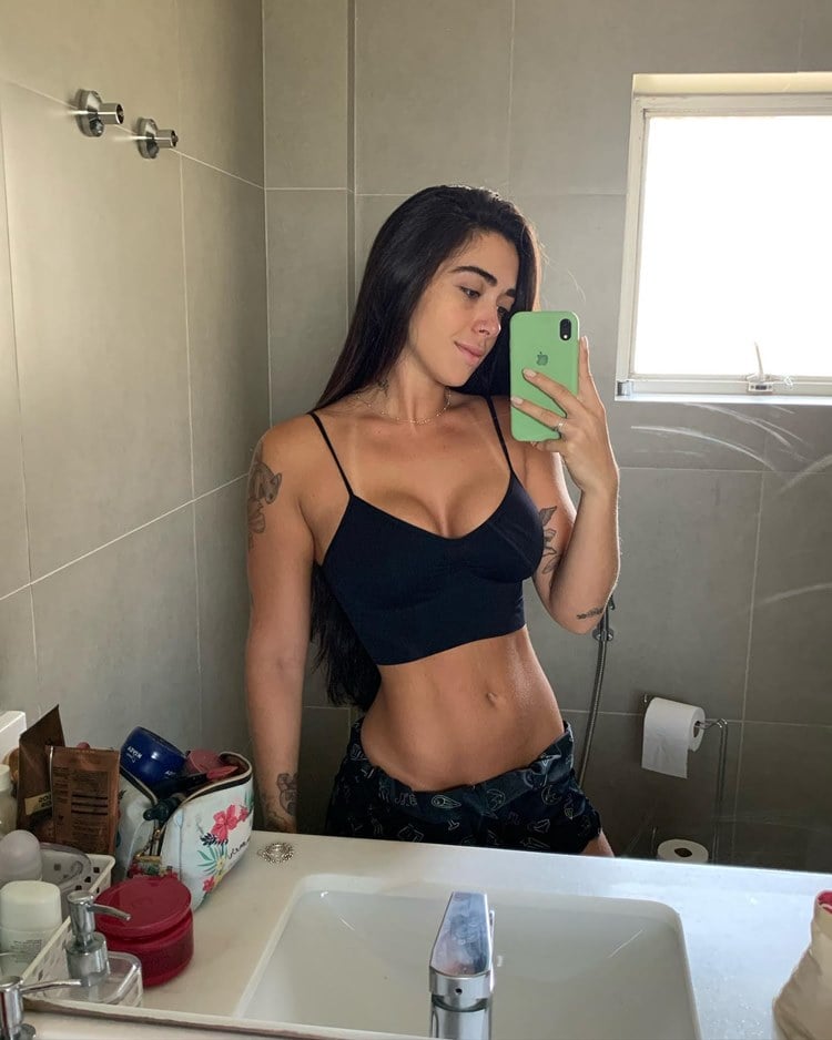 Giovanna Lima do BBB 24 de top preto e shorts em selfie no espelho de banheiro com pia e produtos de beleza