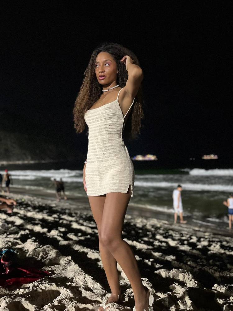 Mulher de pele negra na praia usando vestido curto bege de crochê