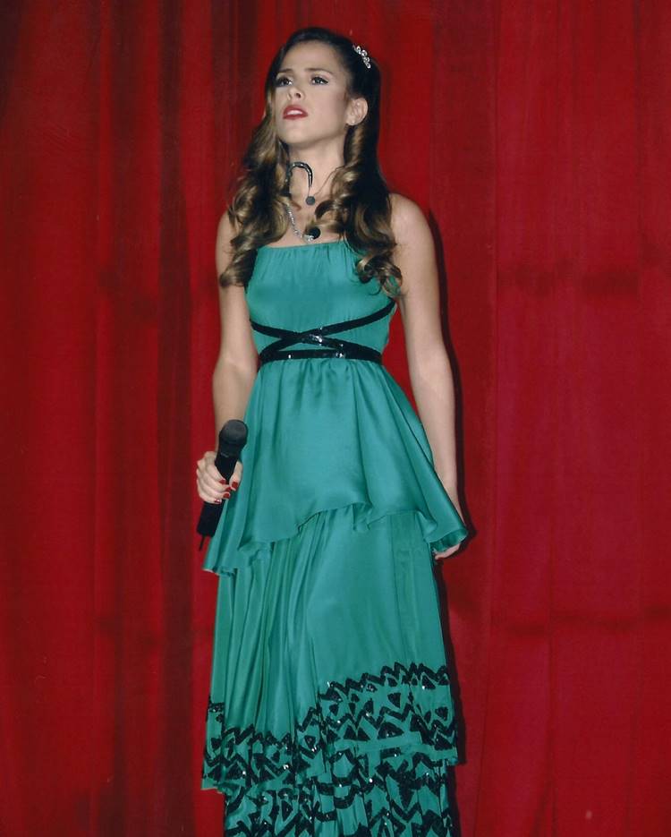 Wanessa Camargo jovem usando vestido longo verde com detalhes em miçangas pretos, segurando microfone em frente à cortina vermelha