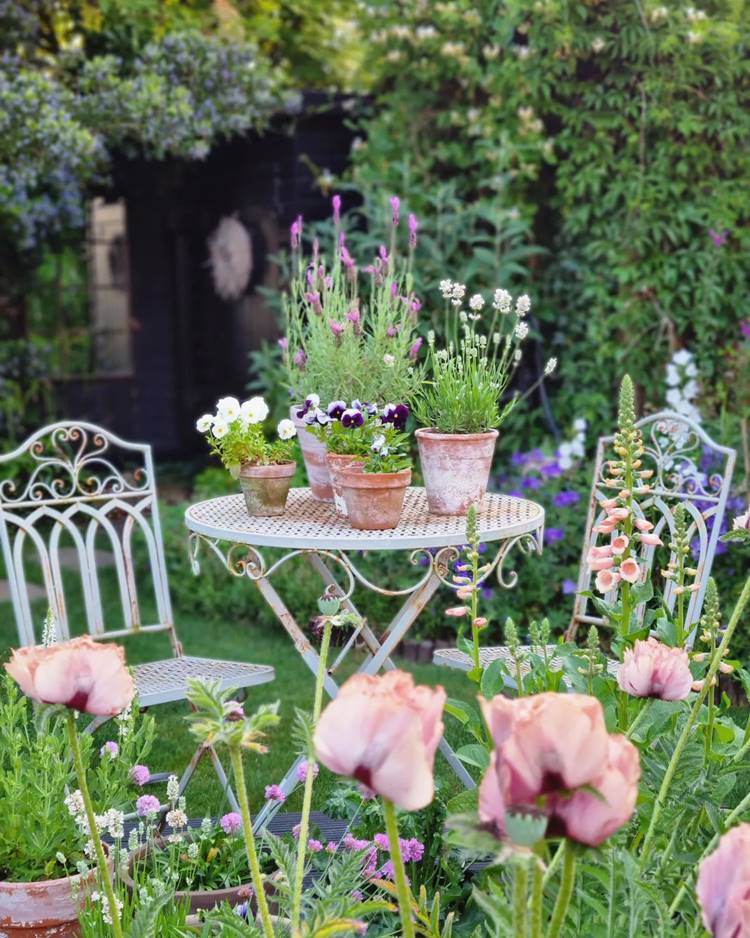 Mesa de ferro em jardim com vasos de plantas com flores lindas e coloridas.