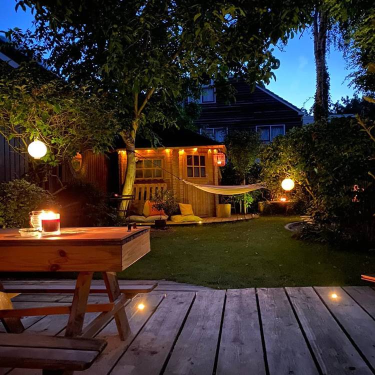 Jardim à noite, com rede, luzes, mesa de madeira e árvores