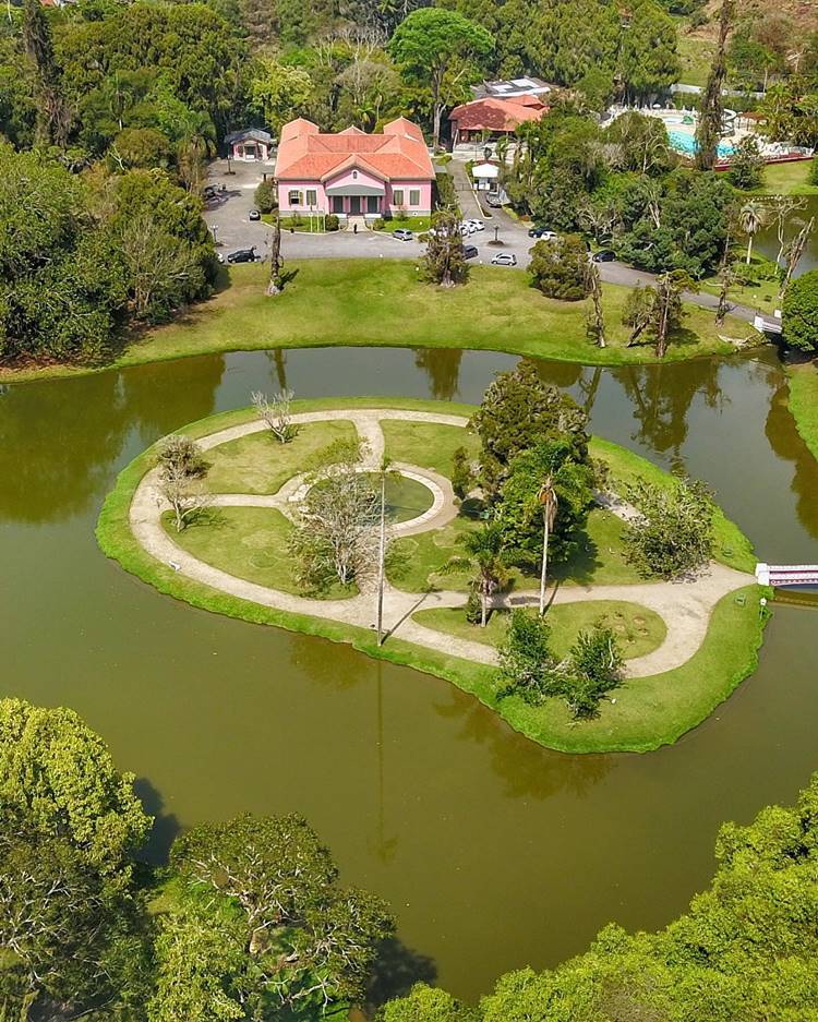 Imagem de drone do Nova Friburgo Country Club. Ilha com lago em volta e casa grande rosa 