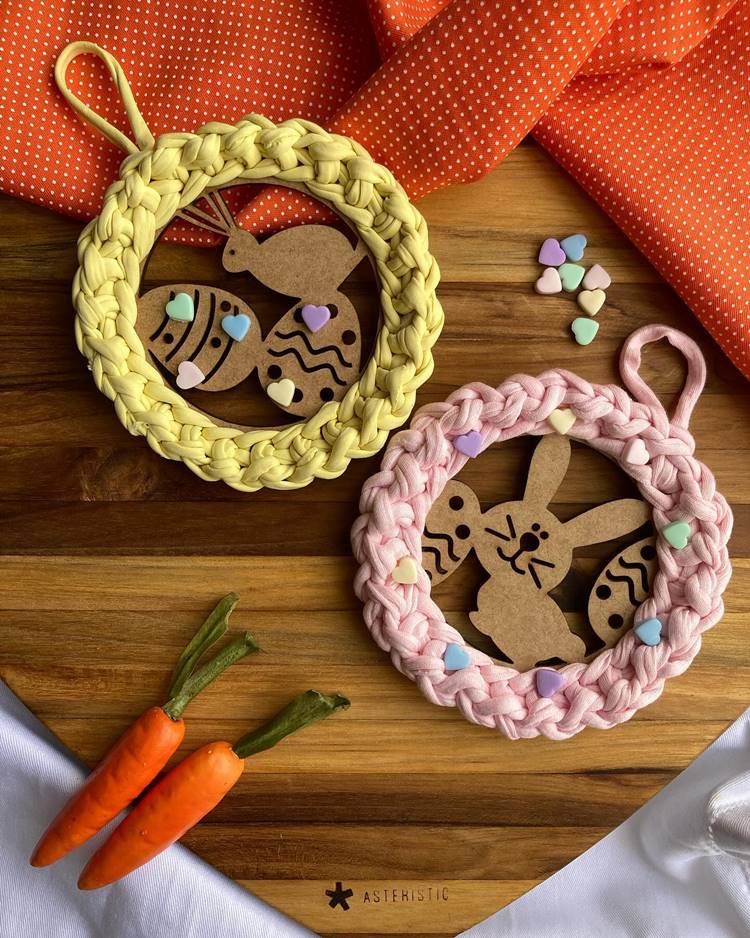Lembrancinha de Páscoa: guirlandinha de crochê com coelhinhos de MDF sobre uma tábua de madeira, decorada com cenouras e corações.

