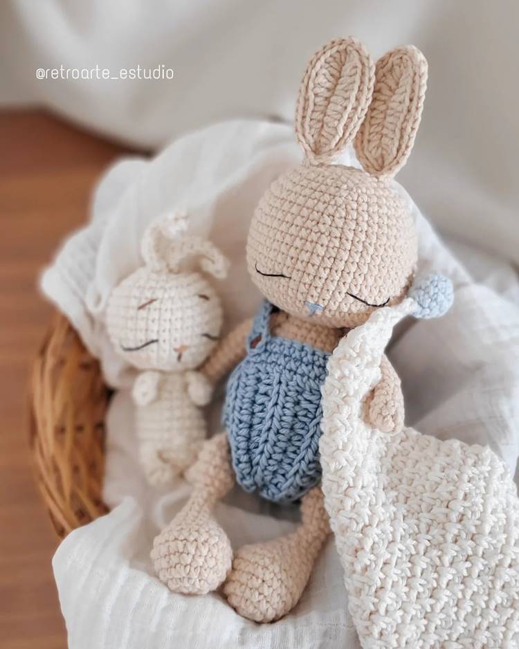 Outra lembrancinha é um coelhinho de crochê acompanhado de uma mantinha de crochê, ambos sobre uma cesta.

